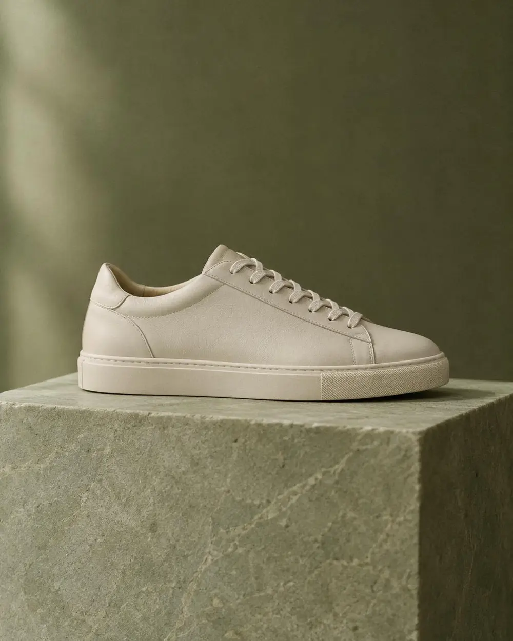 Plain unbranded low-top sneaker in navy canvas photographed straight on against a soft ivory studio floor.