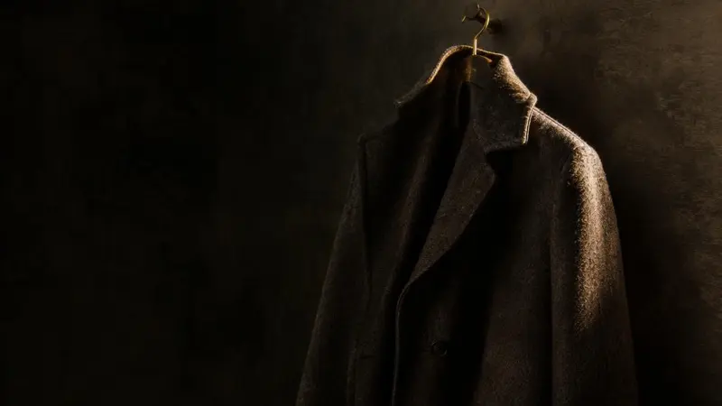 Cappotto di lana appeso a una parete scura, illuminato di lato