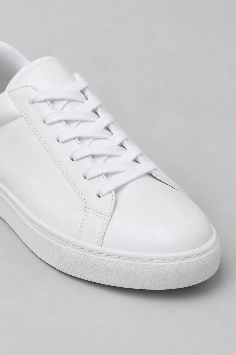 Close-up of an unbranded white low-top sneaker shown against a pale grey background.