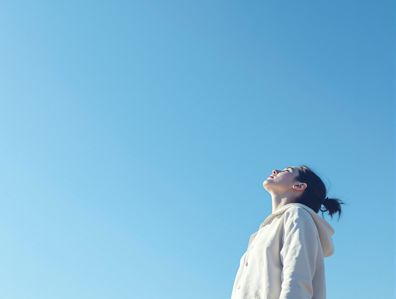 青空を見上げて深呼吸をしている人のシルエット