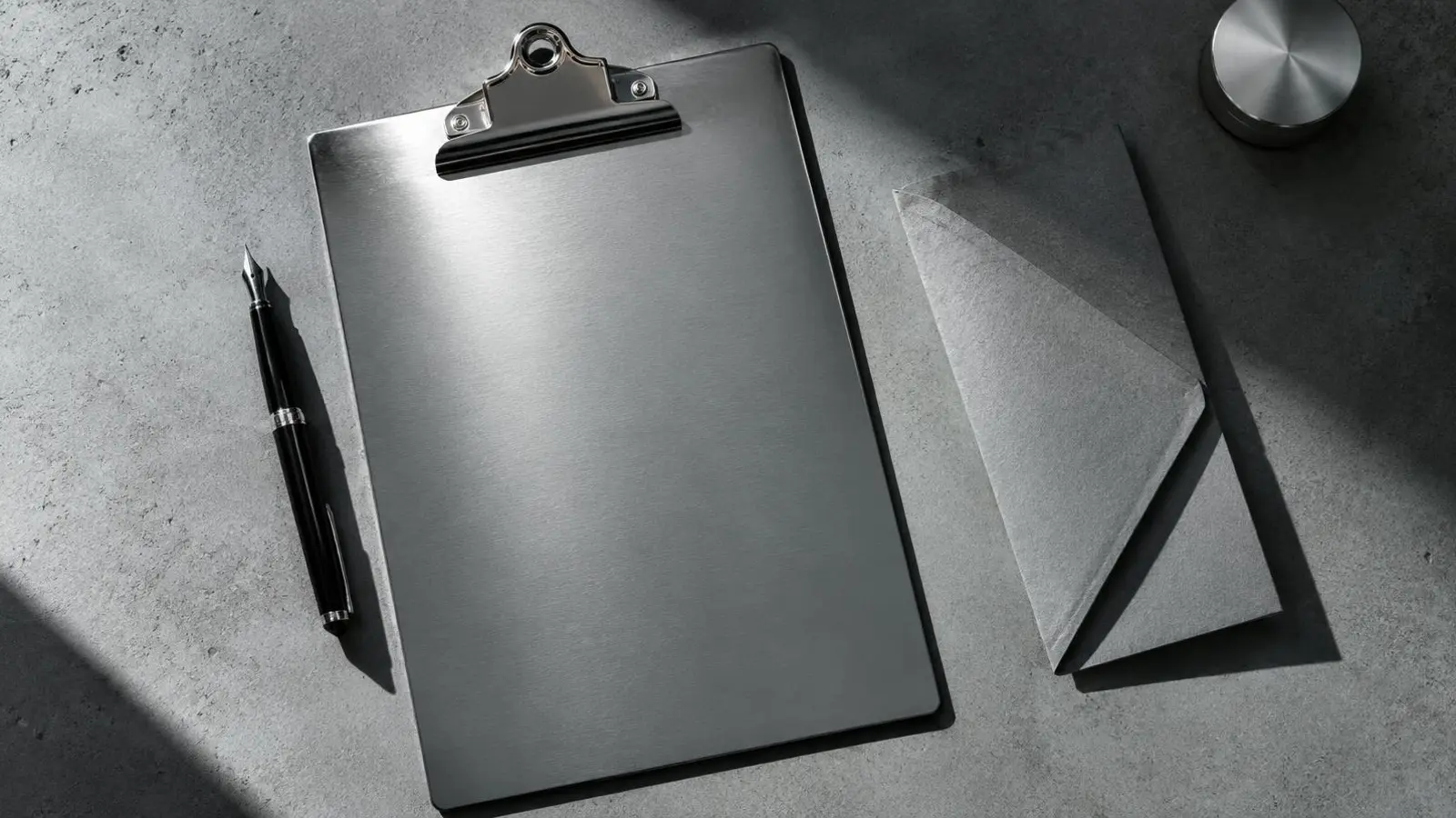 Clipboard, pen and folded grey paper on a cool concrete desk