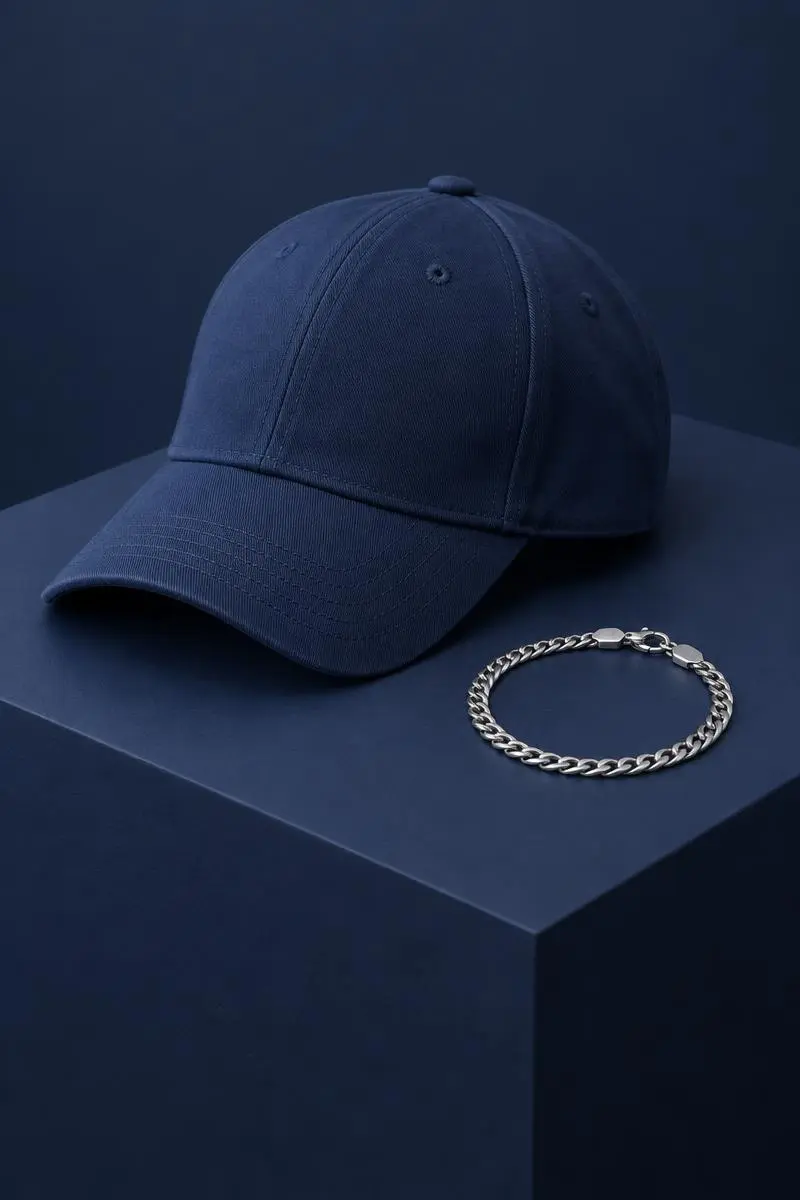 Blank solid-colour baseball cap and a plain chain bracelet on a deep navy display plinth.