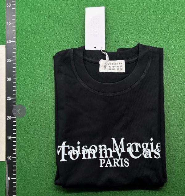 Folded black crew-neck T-shirt with white lettering on a green mat